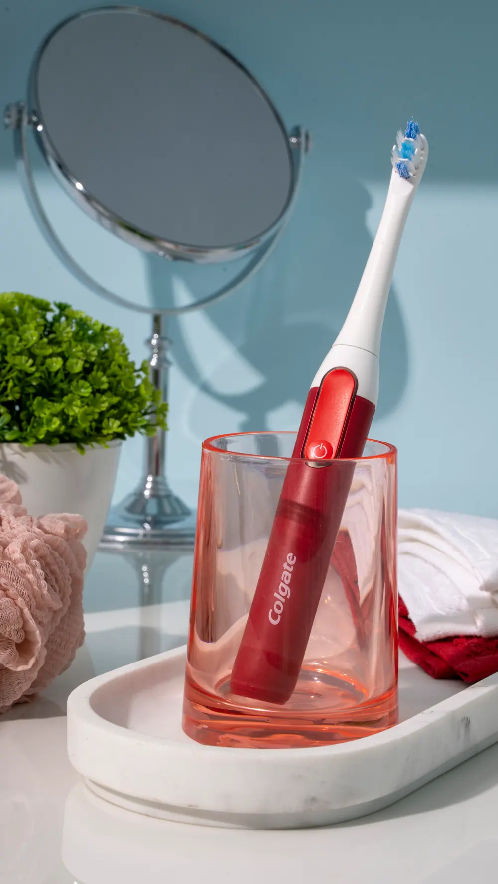 Red toothbrush in a tinted tumbler by a mirror