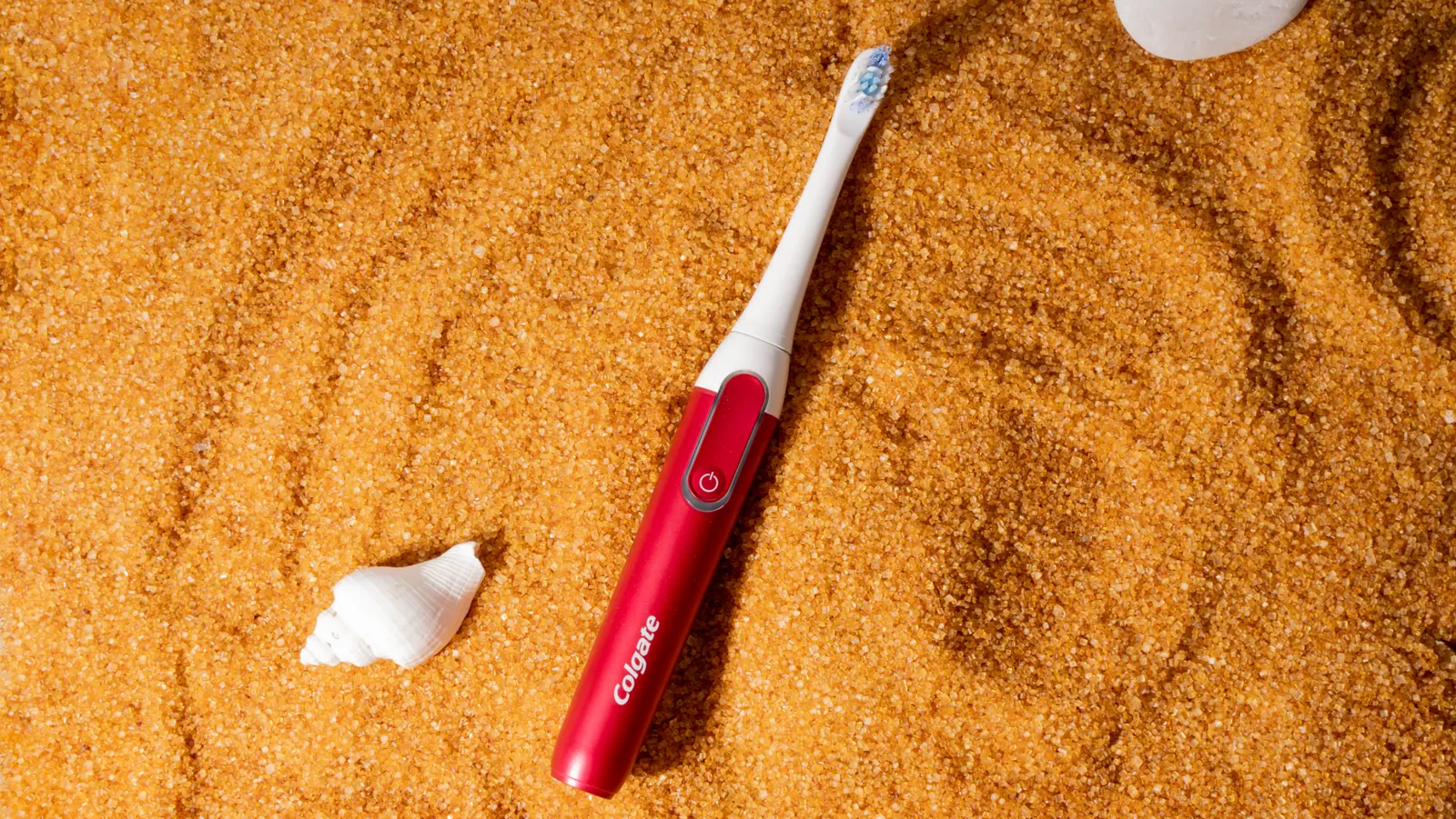 Red toothbrush on sand with a shell